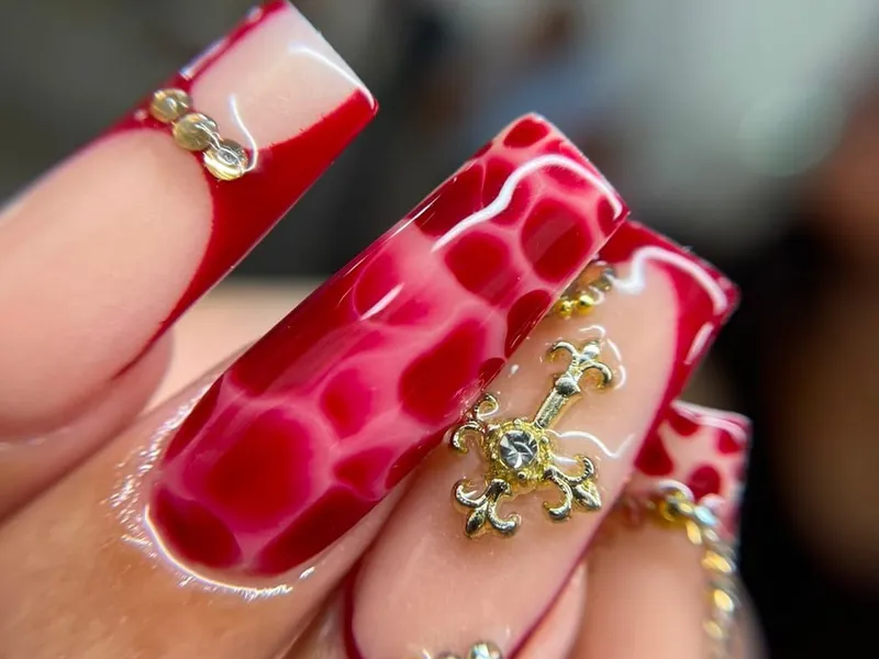 Uñas acrílicas largas en rojo con diseño de pedrería dorada
